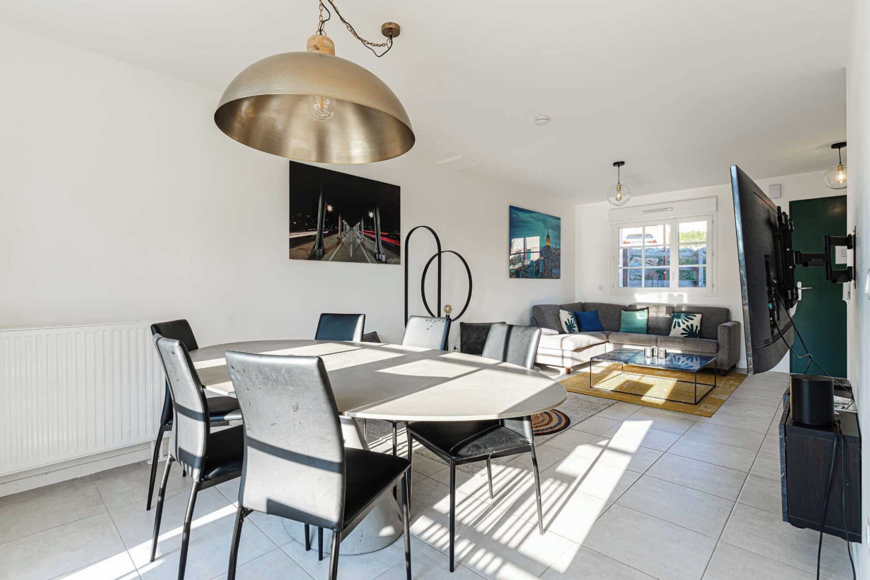 A modern dining area with a large table and chairs, a hanging pendant light, and artwork on the walls.