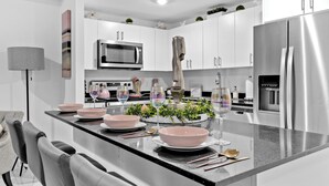 A modern kitchen with white cabinets, stainless steel appliances, and a central island with pink bowls and wine glasses. - Peaceful Dreamscape a spacious family friendly minutes to the Keys & Miami (Princeton)