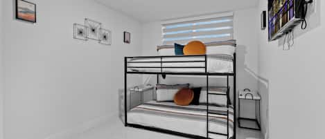 A bunk bed room with a window, a wall-mounted TV, and a small shelf.