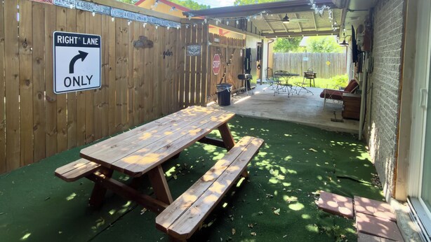 Ein Holzzaun mit einem Schild 'RECHTSBAHNEN NUR', ein Picknicktisch und ein überdachter Patio-Bereich mit Gartenmöbeln.