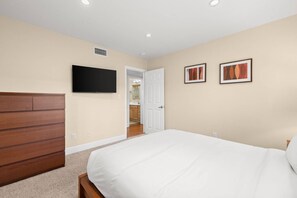 Ein Schlafzimmer mit einem Bett, einem an der Wand montierten Fernseher und zwei gerahmten Bildern.
