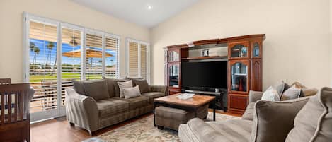 Un salón espacioso con un televisor de pantalla plana grande, un sofá de cuero marrón, un reposapiés a juego y un mueble de madera con puertas de vidrio.