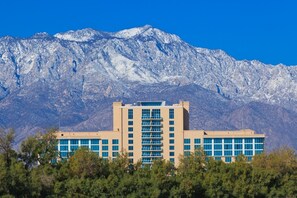A modern building with a central atrium and multiple floors, surrounded by trees and mountains in the background.