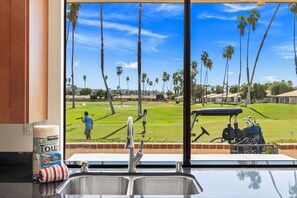 Eine Küche mit Spüle und Fensterblick auf einen Golfplatz.