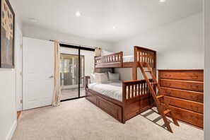 A bedroom with a bunk bed, a wooden dresser, and a sliding glass door leading to a balcony.