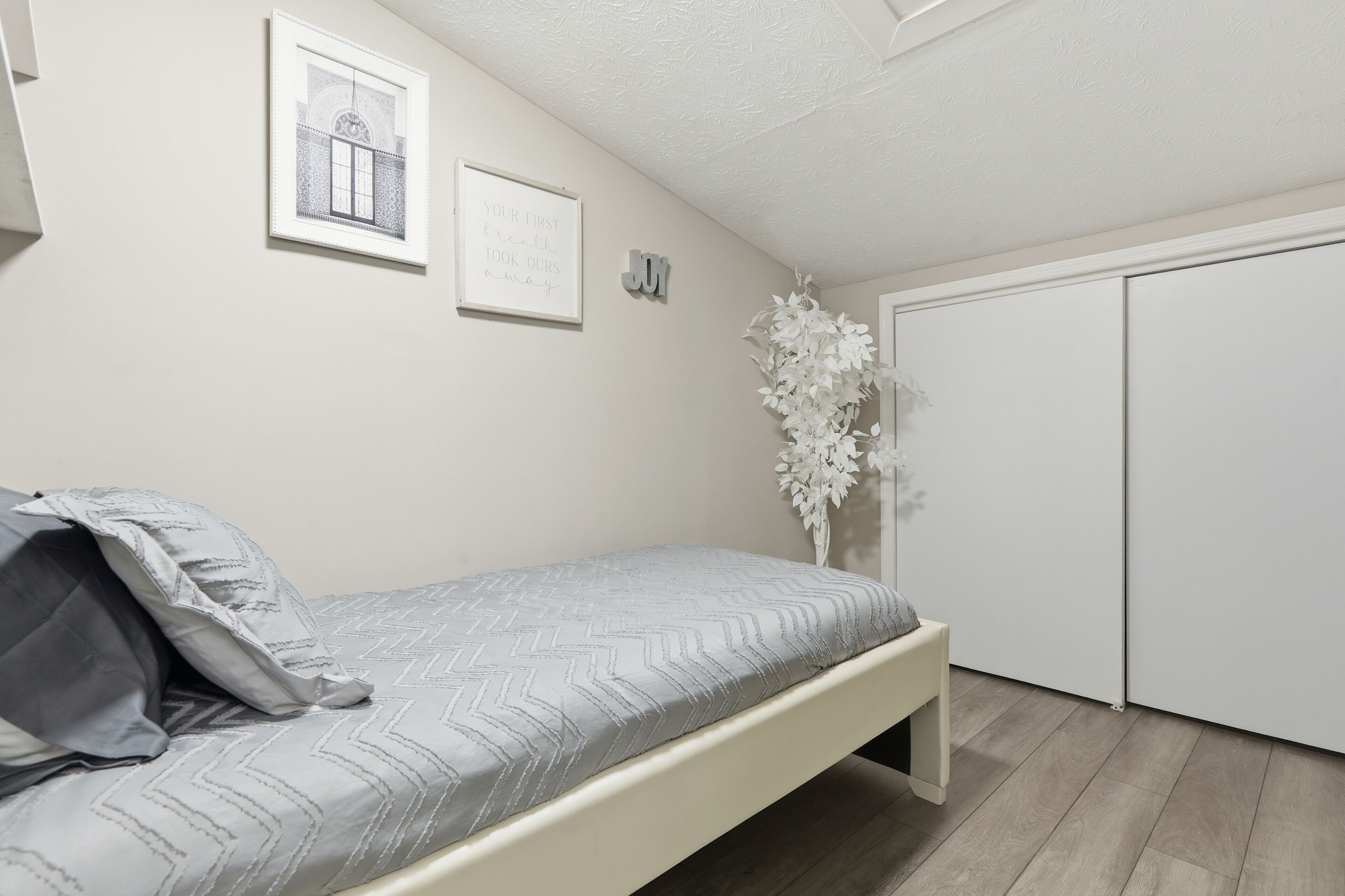 A bedroom with a bed, a wall-mounted picture, a decorative plant, and a wardrobe.