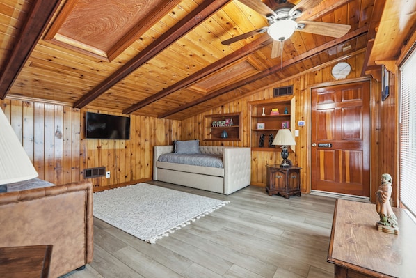 A cozy room with wooden walls and ceiling, a bed, a television, a small table, and a statue. - Spacious 7-bedrooms house with Pool, Close to FT Benning, Malls, Copper Creek (Columbus)