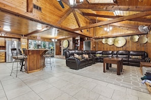 A spacious living area with a large leather sofa, a wooden bar, and a stone floor. - Spacious 7-bedrooms house with Pool, Close to FT Benning, Malls, Copper Creek (Columbus)