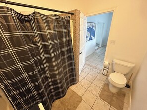 A bathroom with a black and white checkered shower curtain, a white toilet, and a beige tiled floor. - Exact Middle of Downtown Frisco Everything within steps (Frisco)