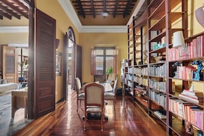 A library with wooden bookshelves, a dining area with chairs, and a large window. - Grand Historic Mansion in Old SJ | Patio + Rooftop (San Juan)