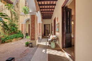 A covered outdoor corridor with a brick floor, a wooden ceiling, and a door leading to a room. - Grand Historic Mansion in Old SJ | Patio + Rooftop (San Juan)