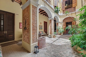 A courtyard with a brick column, a wooden door, and potted plants. - Grand Historic Mansion in Old SJ | Patio + Rooftop (San Juan)