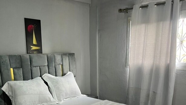 Ein Schlafzimmer mit einem großen Bett, einem Nachttisch, einem Wandbild und einem Fenster mit Vorhängen.
