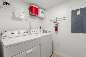 Ein Waschraum mit einer Whirlpool Waschmaschine und einem Trockner, einem roten Warmwasserbereiter und einem an der Wand montierten Feuerlöscher.