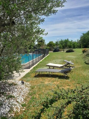 A backyard with a swimming pool, two lounge chairs, and a covered area.