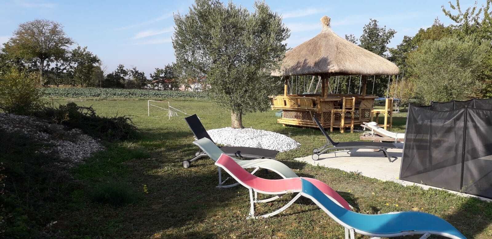 Un kiosque avec un toit de chaume, une pelouse avec des poteaux de but et deux chaises longues.