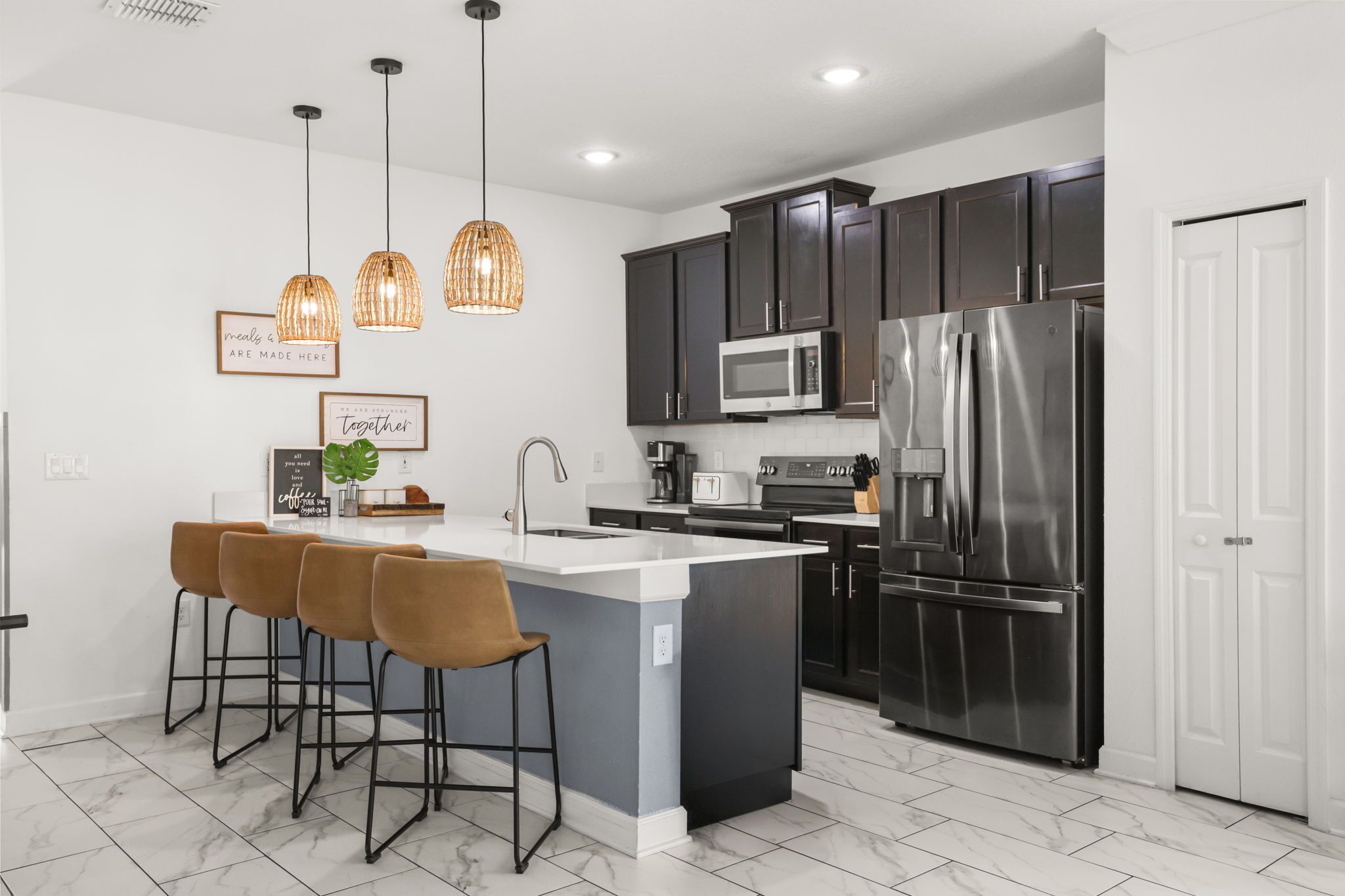 A modern kitchen with a central island, bar stools, stainless steel appliances, and pendant lighting.