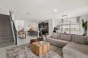 A modern living room with a sofa, coffee table, and a staircase. - Championsgate Near Disney/ Lazy River & Resort 5 BD/ 4.5 BA (1098 SS) (Davenport)