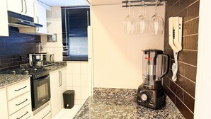Una cocina compacta con horno integrado, microondas y licuadora sobre la encimera.