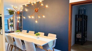 Un comedor con una mesa larga, sillas, una lámpara de araña moderna y una pared azul decorativa.