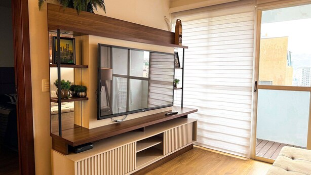 Una sala de estar con una televisión de pantalla plana montada en una consola de madera, un suelo de vidrio corredero y vistas a la ciudad.