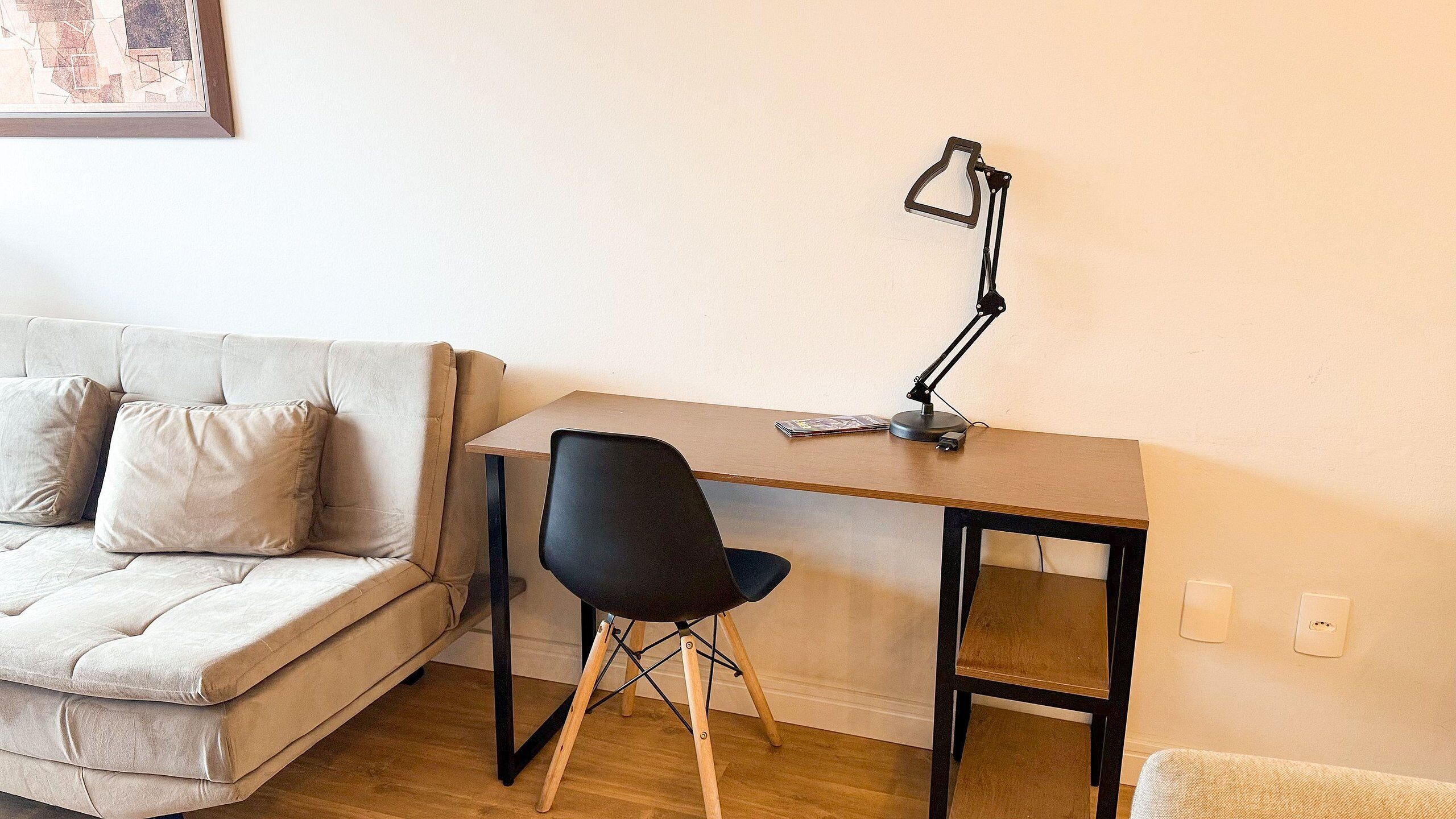 Una habitación pequeña y amoblada con sofá, escritorio, silla y lámpara de escritorio.