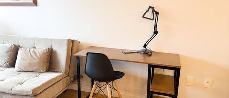 Una habitación pequeña y amoblada con sofá, escritorio, silla y lámpara de escritorio.