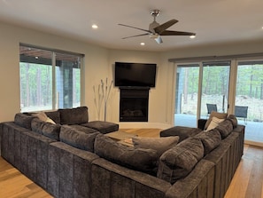 A modern living room with a sectional sofa, a fireplace, a flat-screen TV, and large windows offering a view of the outdoors. - Modern Mountain Retreat in the Pines (Flagstaff)