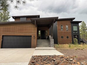 A modern two-story house with a garage, a covered front porch, and a staircase leading to the second floor. - Modern Mountain Retreat in the Pines (Flagstaff)