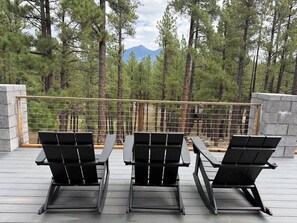 A deck with three black lounge chairs and a stone wall, overlooking a forest and a mountain. - Modern Mountain Retreat in the Pines (Flagstaff)