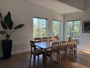 A dining area with a wooden table and chairs, large windows, and a potted plant. - Modern Mountain Retreat in the Pines (Flagstaff)