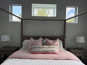 A bedroom with a four-poster bed, two bedside lamps, and a window with a view of trees. - Modern Mountain Retreat in the Pines (Flagstaff)