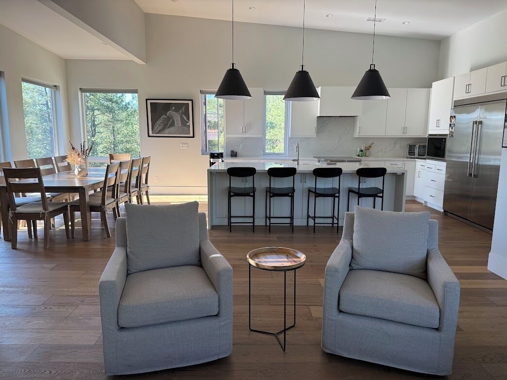 A modern kitchen with white cabinets, a stainless steel refrigerator, and a dining area with a table and chairs.