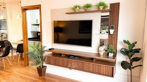 Una sala de estar moderna con un televisor de pantalla plana grande, estanterías de madera y varias plantas en macetas.