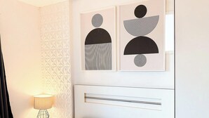 A room with a geometric-patterned wall, a bed with a white headboard, a bedside table with a lamp, and abstract artwork on the wall. - ASA Apartamento Cartagena Oktoberfest (Blumenau)