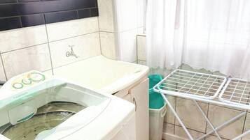 Un área de lavandería con lavadora, tendedero y pared de azulejos.