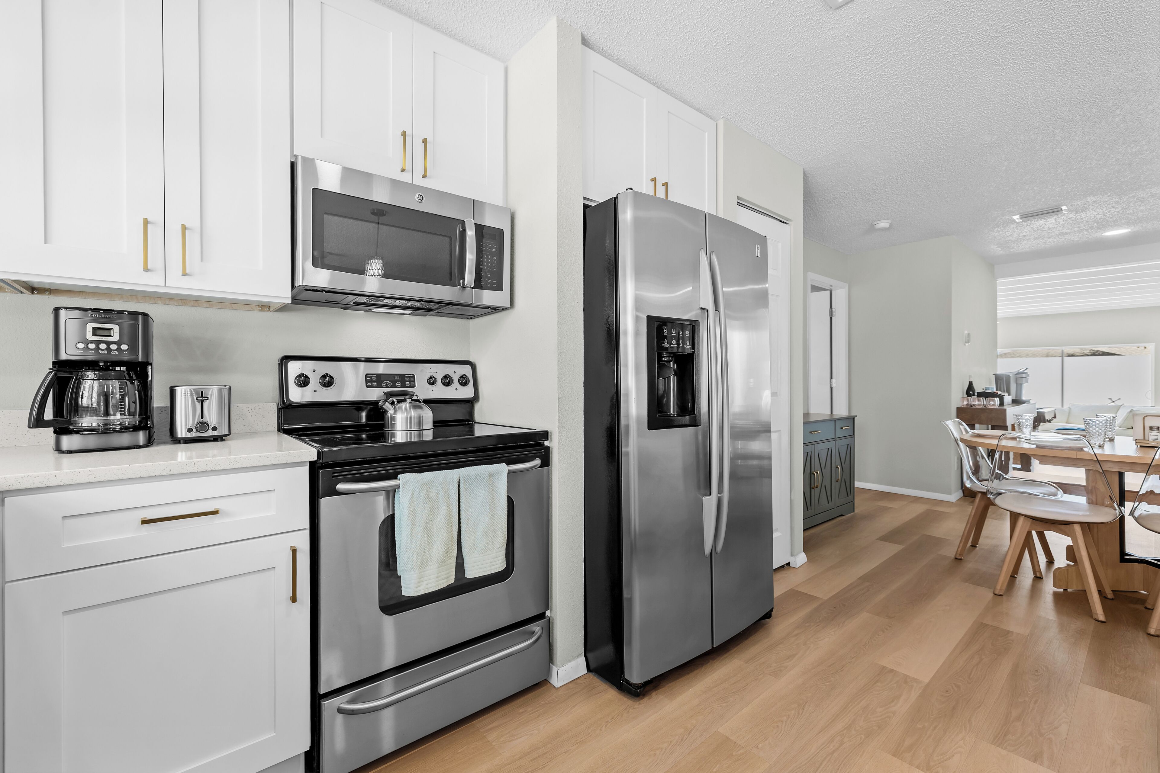 A modern kitchen with stainless steel appliances, white cabinetry, and a wooden dining table.