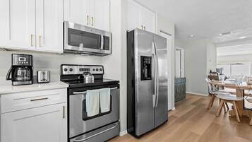 A modern kitchen with stainless steel appliances, white cabinetry, and a wooden dining table.