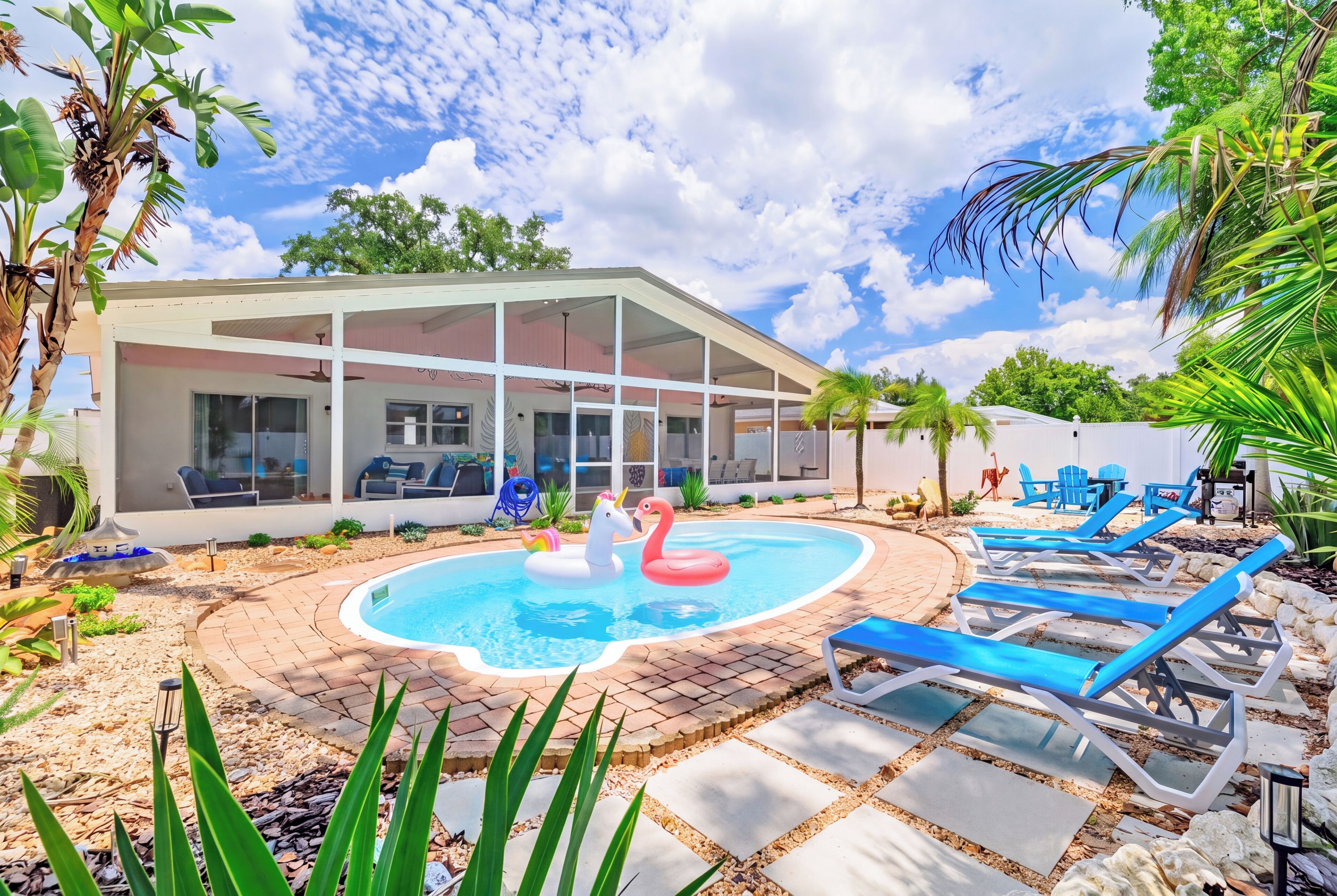 A pool area with lounge chairs and a house with large windows.