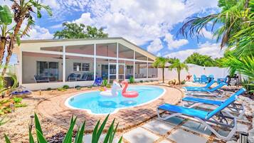 A pool area with lounge chairs and a house with large windows.