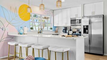 A modern kitchen with white cabinetry, a stainless steel refrigerator, a large island with bar stools, and pendant lighting.