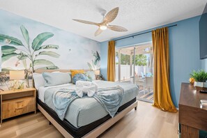 Ein Schlafzimmer mit Bett, Nachttisch, Deckenventilator und Blick ins Freie.