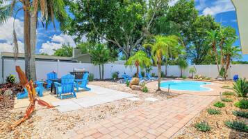A backyard with a pool, patio furniture, and a barbecue area.