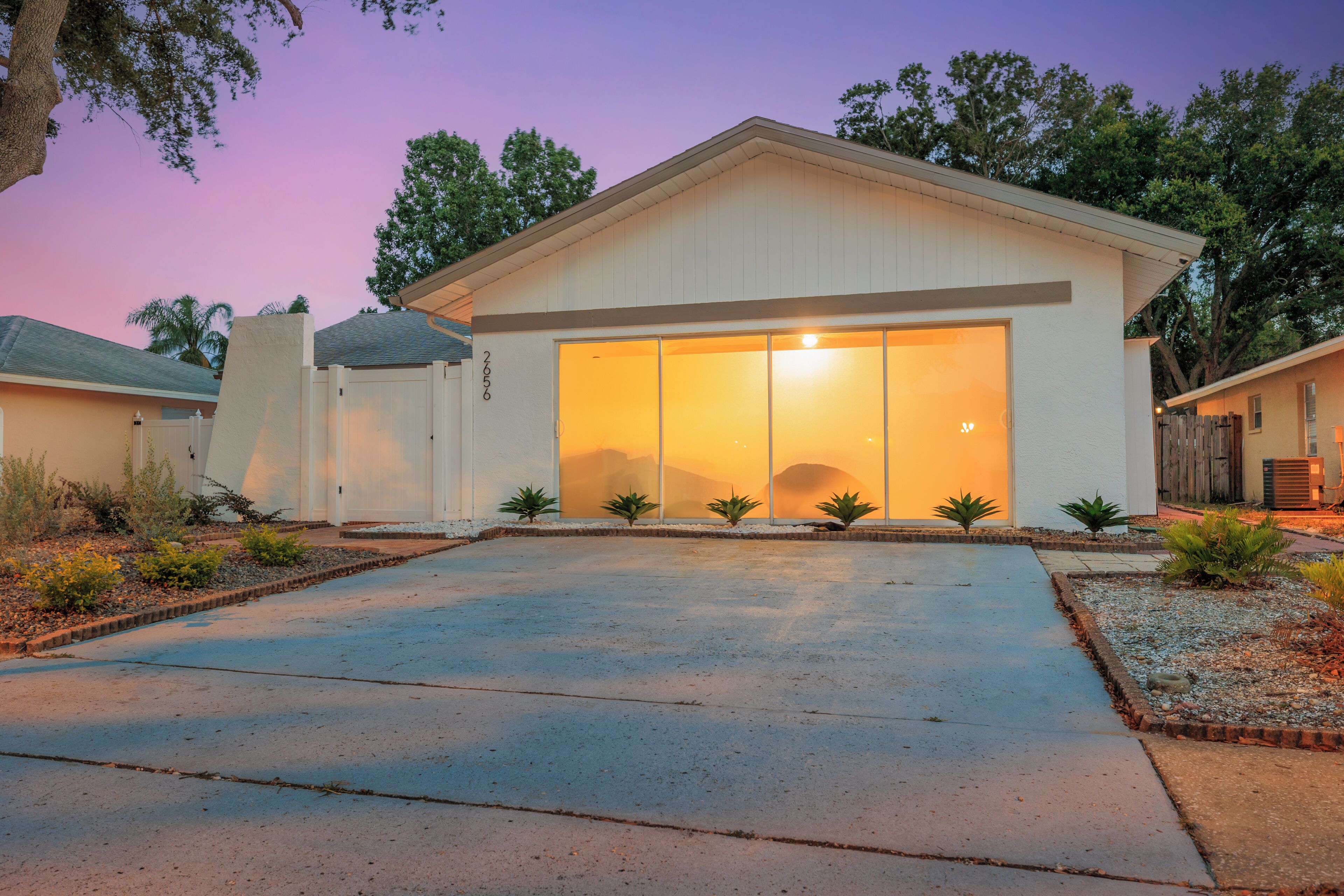 A modern single-story house with a large garage door, surrounded by a landscaped garden with small shrubs and a gravel driveway.