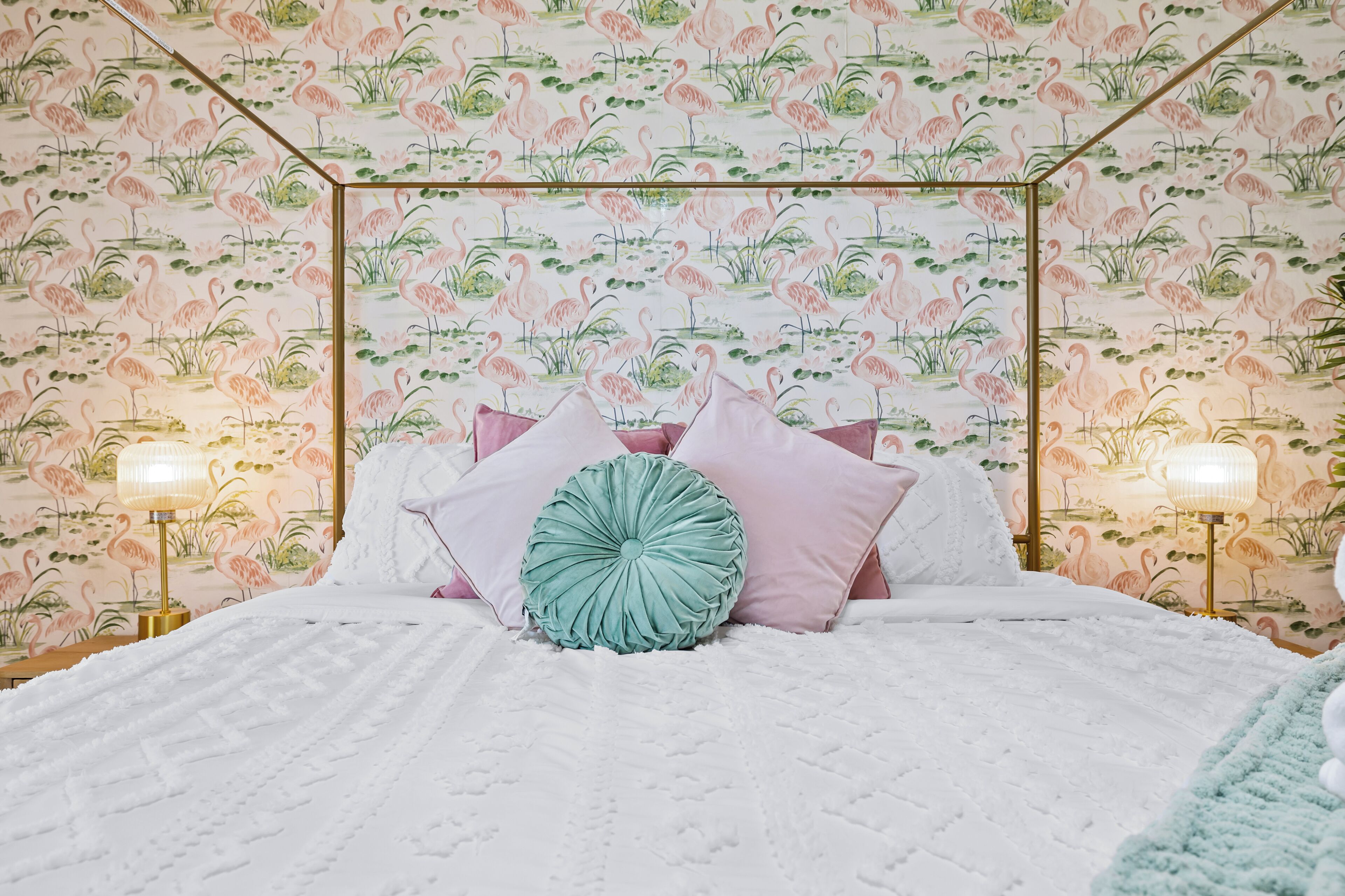 A bedroom with a floral wallpaper, a bed with multiple pillows, and bedside lamps.