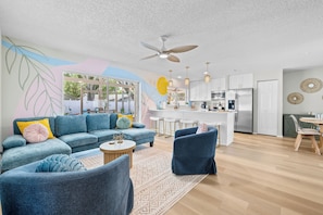 A modern living room with a sofa, chairs, and a coffee table. There is a kitchen area with a refrigerator, microwave, and bar stools. - NEW Saltwater Pool, Game Room, Arcades, Huge Lanai, Firepit (Palm Harbor)