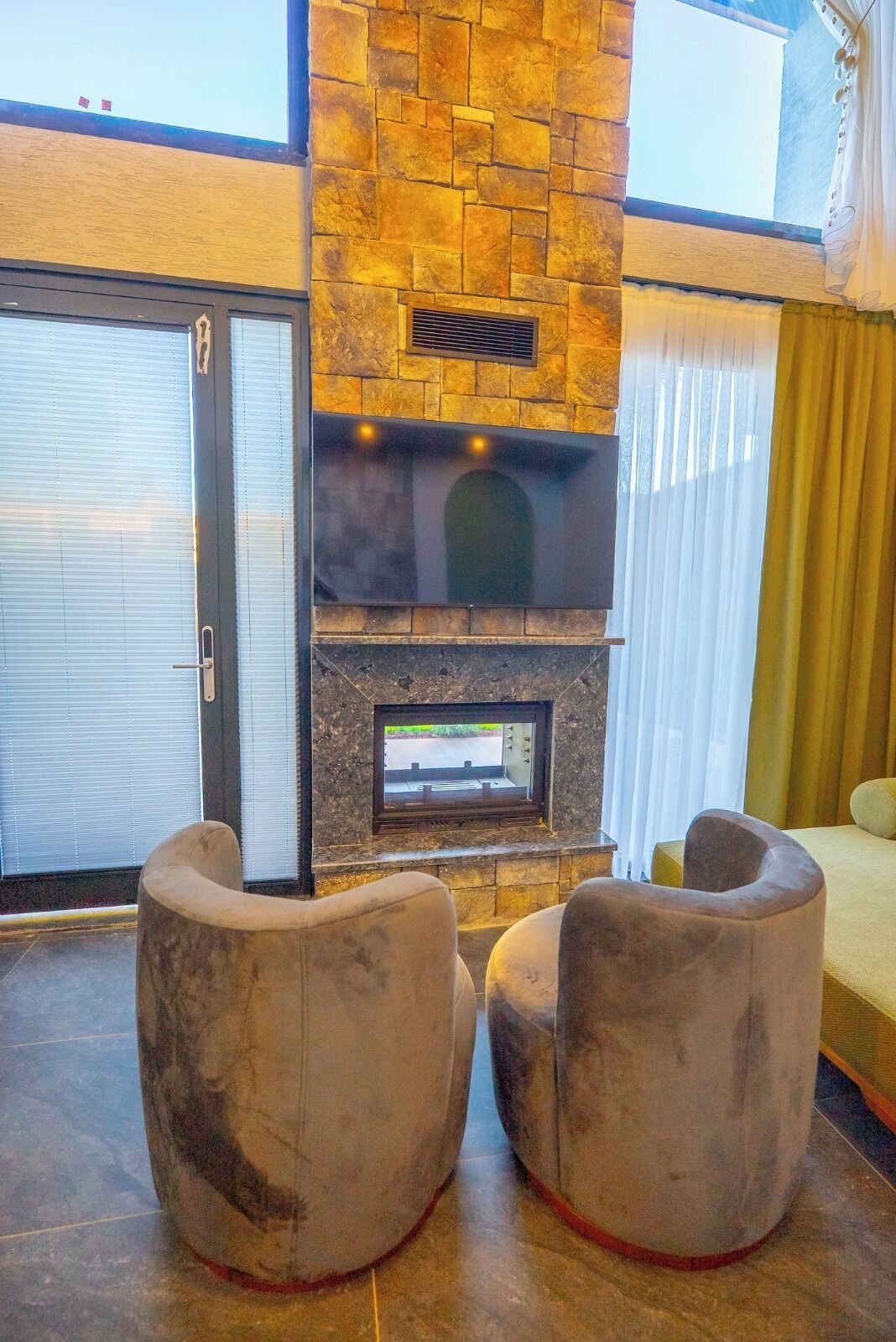 Un espace de vie moderne avec une cheminée en pierre, deux fauteuils et une vue sur l’extérieur.
