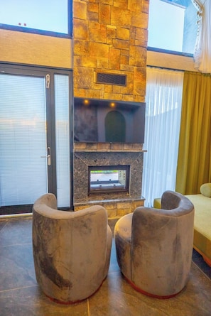 A modern living area with a stone fireplace, two armchairs, and a view of the outdoors.