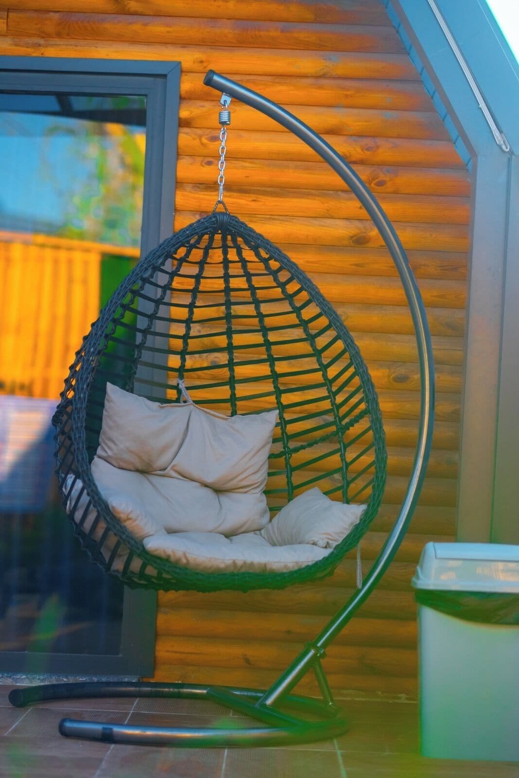 A green hanging chair with cushions in a wooden cabin setting.