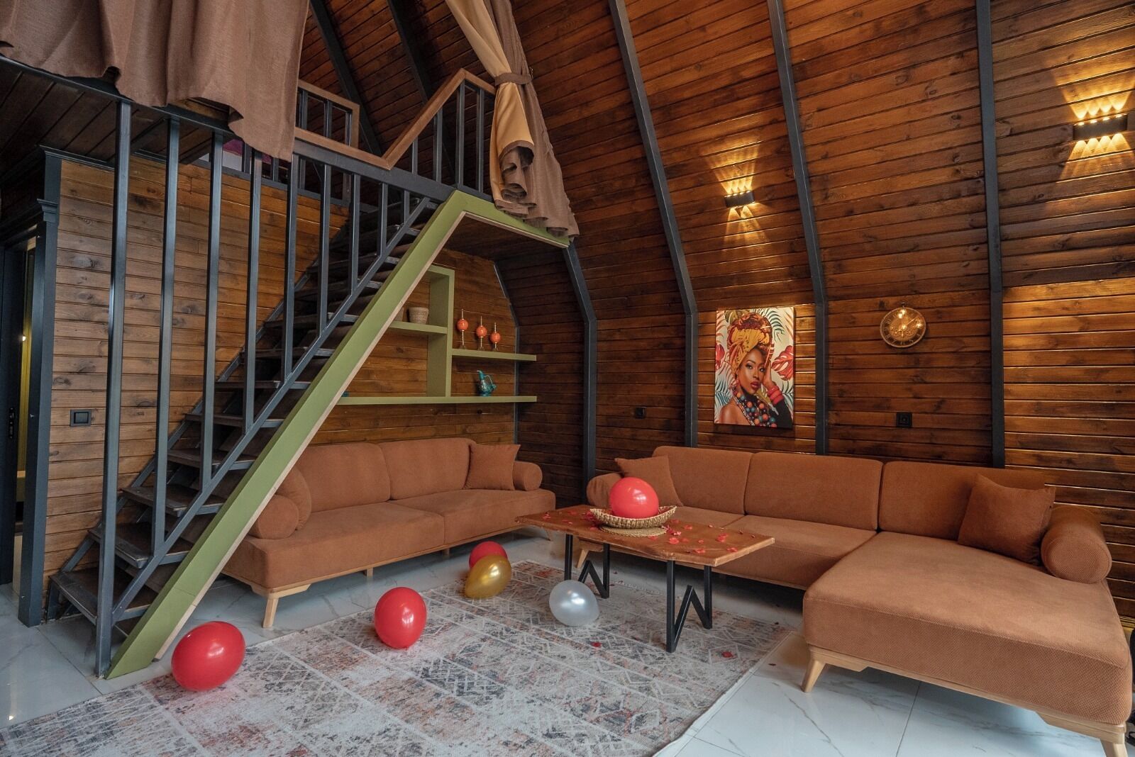 A loft-style room with a wooden ceiling, a staircase, a sofa, a table, and a painting.